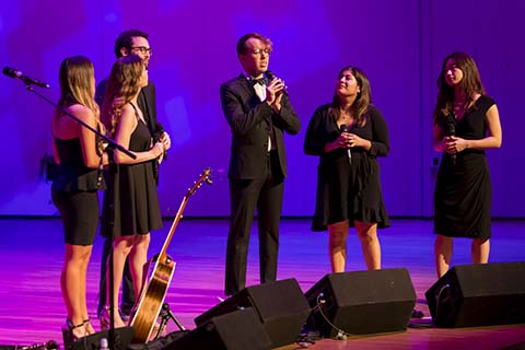 A vocal group wearing black forma attire perform on a stage during an event